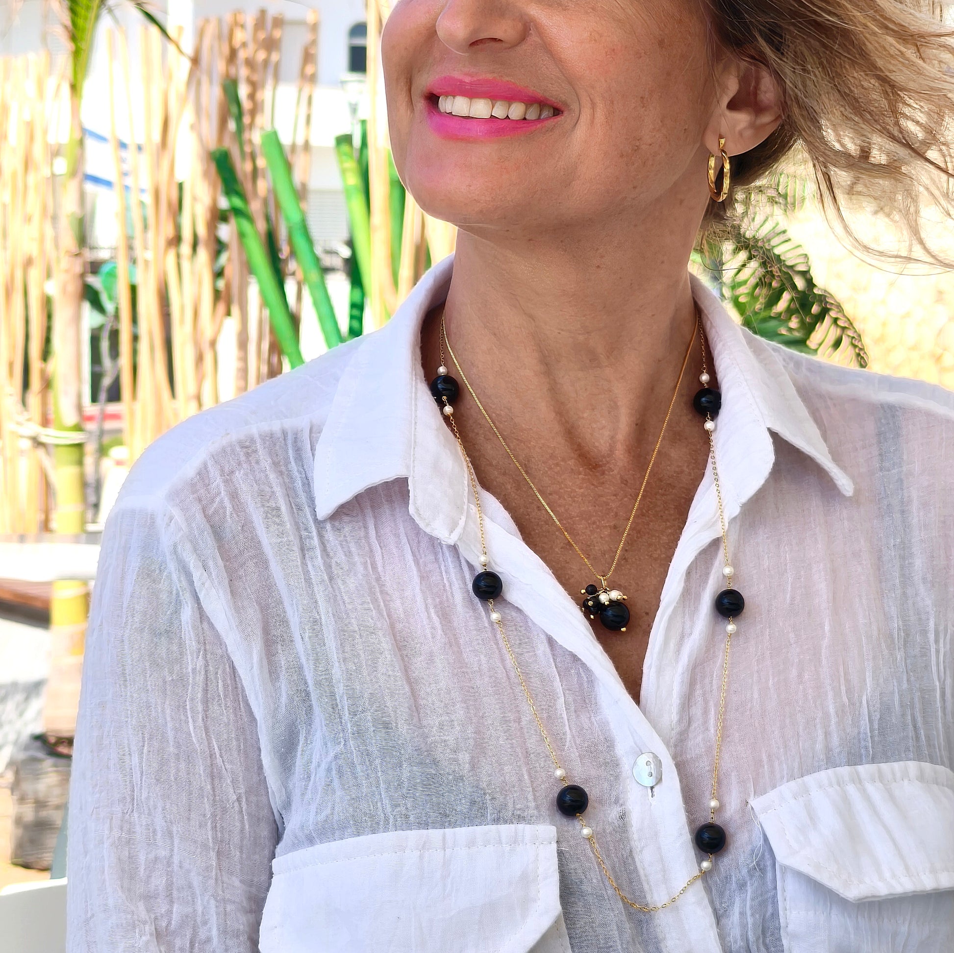 Woman wearing a white shirt with a necklace featuring black beads outdoors.